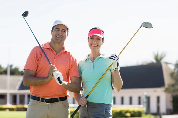 Smiling couple holding golf clubs