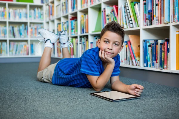 Boy lying with tablet in school library
