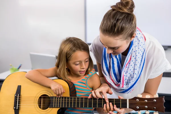 Teacher assisting girl to play guitar