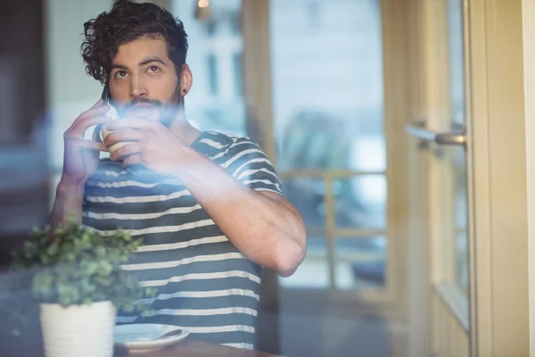 Man sipping coffee while talking on cellphone