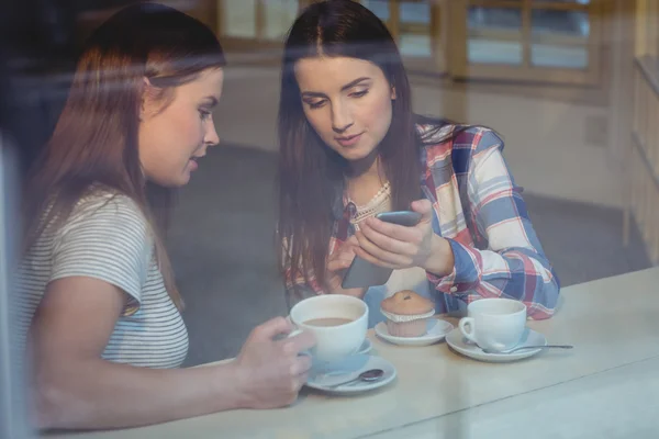Woman showing cellphone to friend at cafe