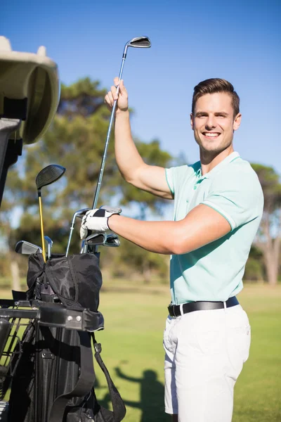 Smiling man putting golf club in bag