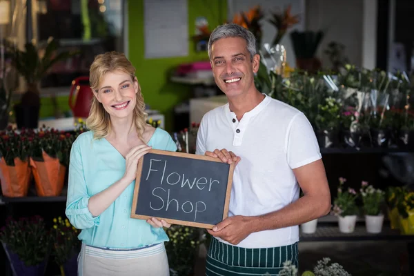 Smiling florists holding flower shop sign on slate