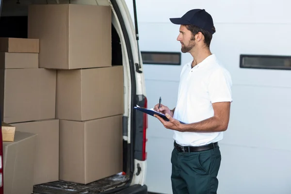 Delivery man is looking his goods and holding a clipboard