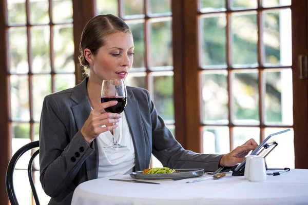 Woman using a tablet and drinking wine