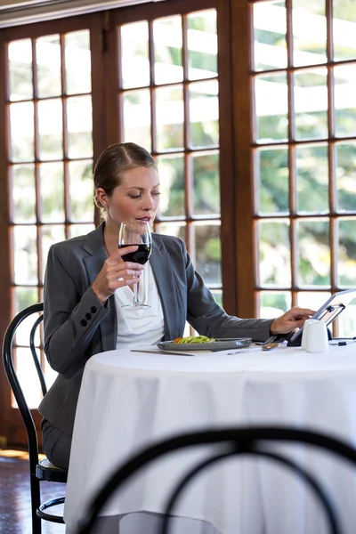 Woman using a tablet and drinking wine