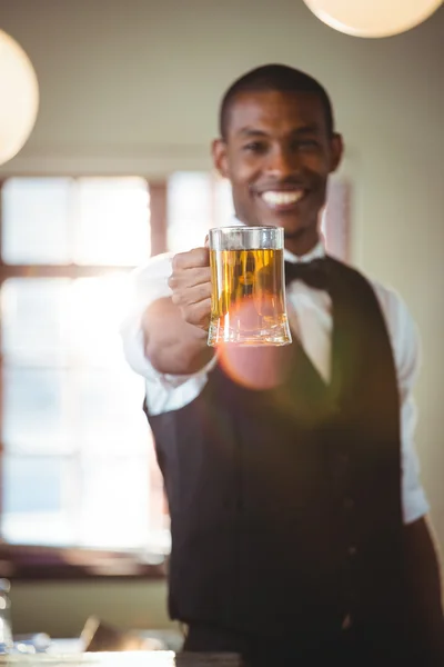 Smiling bartender offering a glass of beer at bar counter