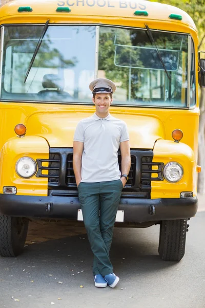 Smiling bus driver leaning with hands in pocket in front of bus