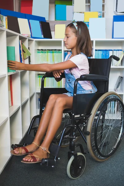 Disabled school girl selecting a book from bookshelf in library