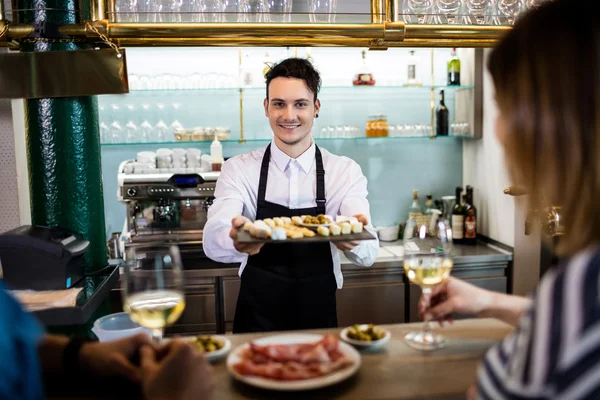 Young bartender serving food to customers