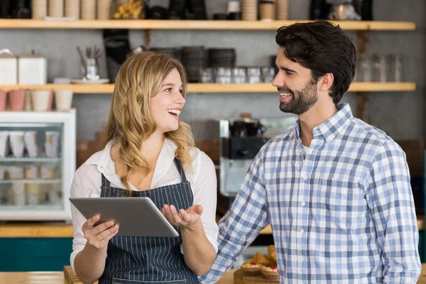 Smiling man and waitress standing at counter using digital table