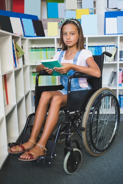 Disabled school girl on wheelchair holding a books in library