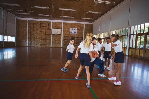Sports teacher and school kids playing basketball