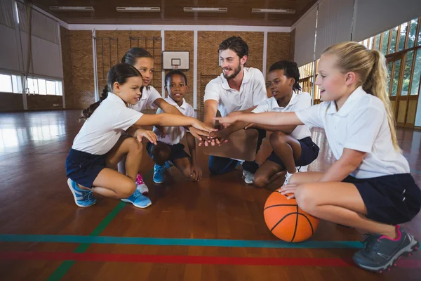 Sports teacher and school kids forming hand stack in basketball court