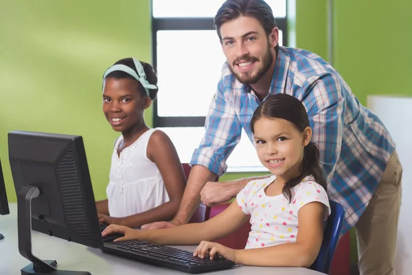 Teacher assisting schoolgirls in learning computer