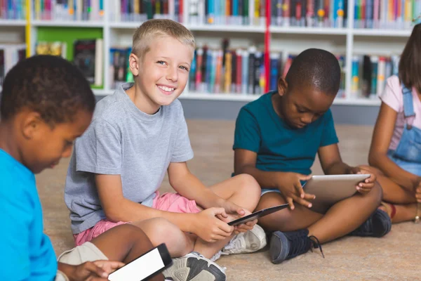 School kids sitting on floor using digital tablet in library