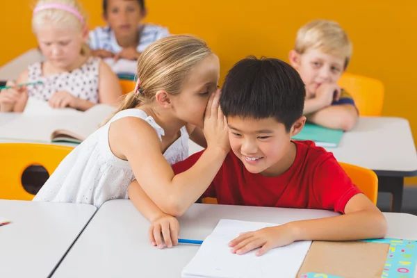 Schoolgirl whispering into her friend s ear in classroom
