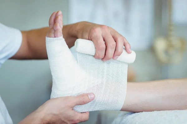 Physiotherapist putting bandage on injured feet