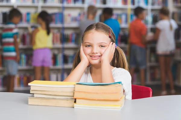Portrait of girl sitting with pile of books in library