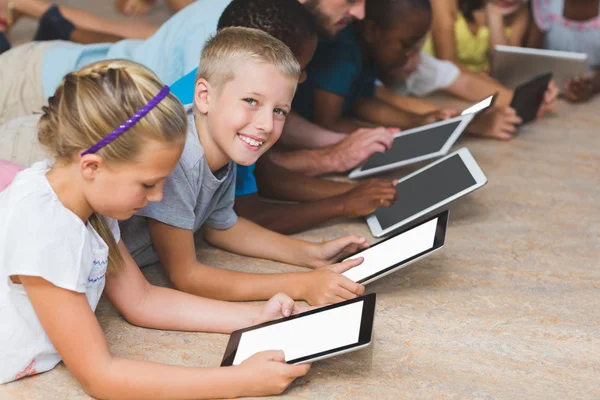 Teacher and kids lying on floor using digital tablet in library