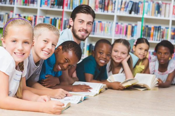 Teacher and kids lying on floor reading book in library