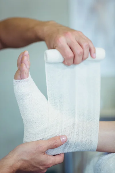 Physiotherapist putting bandage on injured feet of patient