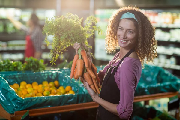 Smiling female staff holding bunch of carrots