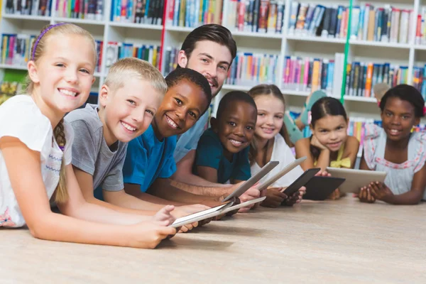 Teacher and kids lying on floor using digital tablet in library