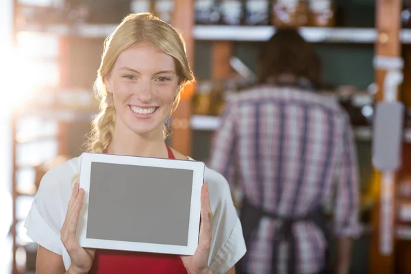 Smiling female staff showing digital tablet in supermarket