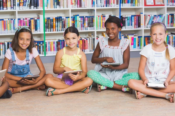 School kids sitting on floor using digital tablet in library