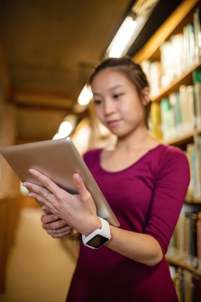 Young woman using digital tablet in library