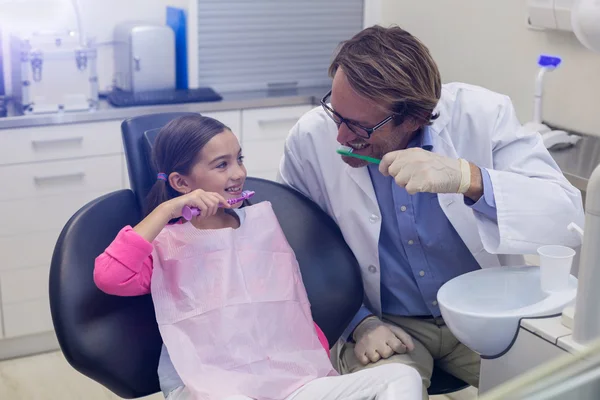 Smiling dentist and patient brushing their teeth