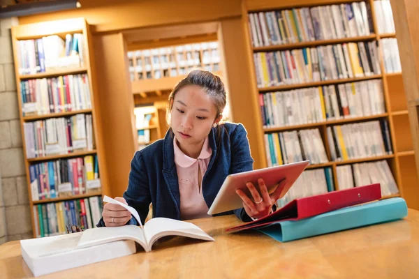 Young woman using digital tablet while studying in library