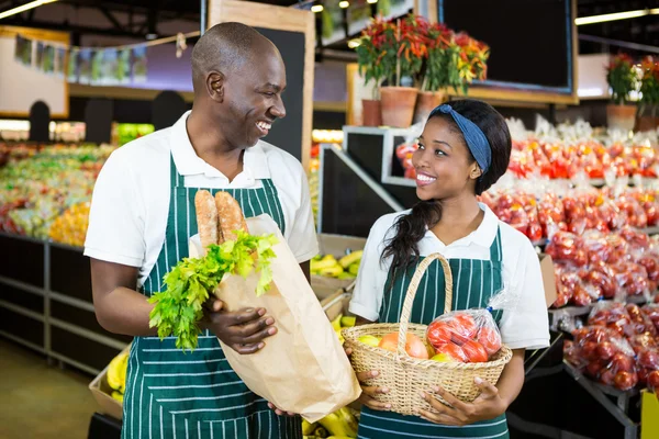 Smiling staffs holding basket and paper bag of vegetables