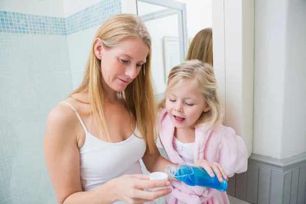 Woman pouring blue mouthwash with daughter