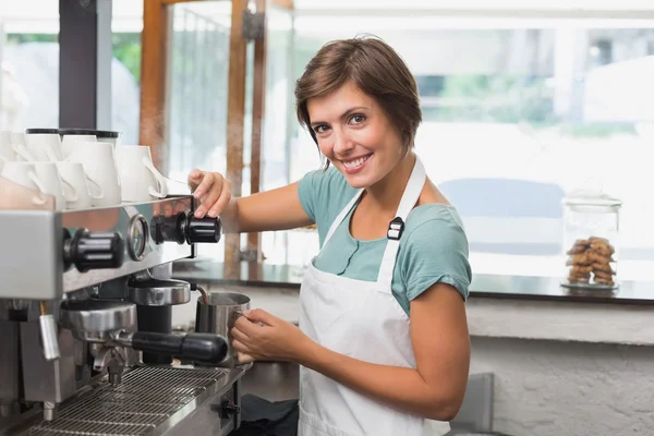 Pretty barista steaming jug of milk at coffee machine