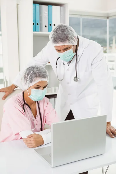 Doctors wearing surgical masks while using laptop at medical office