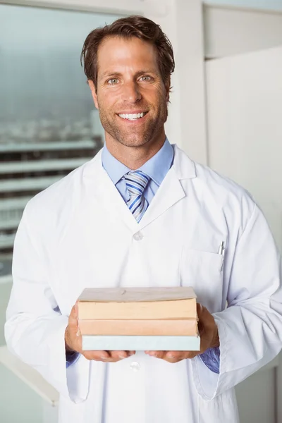 Smiling doctor holding books in medical office
