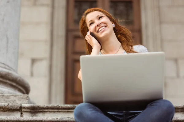 Smiling girl calling with her mobile phone and using laptop