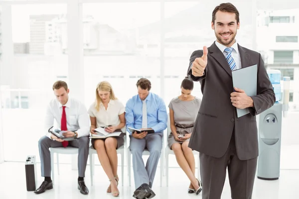 Businessman gesturing thumbs up against people waiting for interview