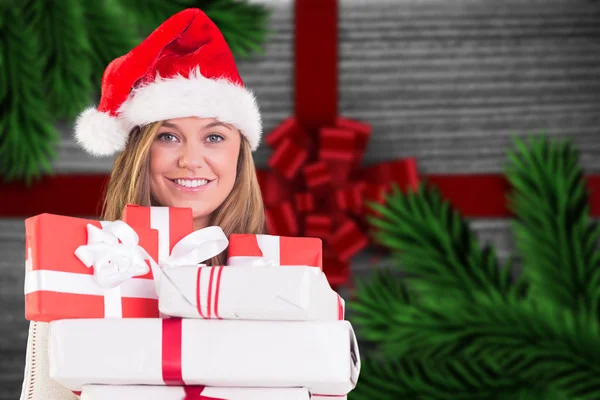 Composite image of festive blonde holding pile of gifts