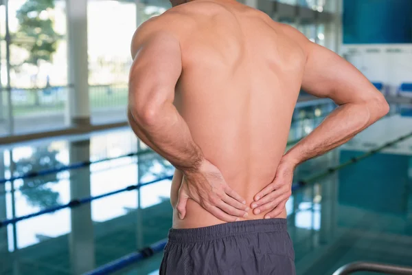 Mid section of shirtless fit swimmer with back ache by pool