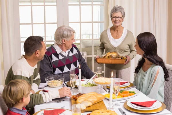 Grandmother holding turkey roast with family at dining table