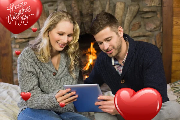 Couple using tablet pc in front of lit fireplace