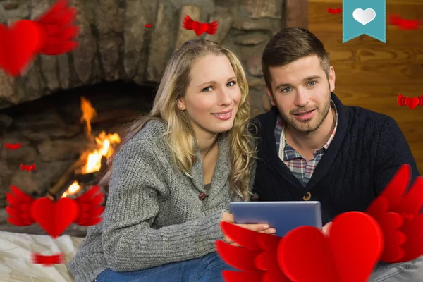 Couple using tablet pc in front of lit fireplace