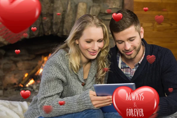 Couple using tablet pc in front of lit fireplace