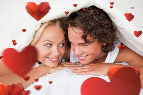 Couple under a duvet with a knowing smile