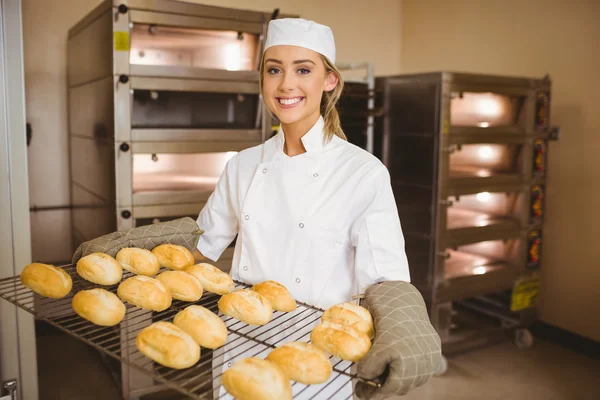 Baker smiling at camera holding rack of rolls