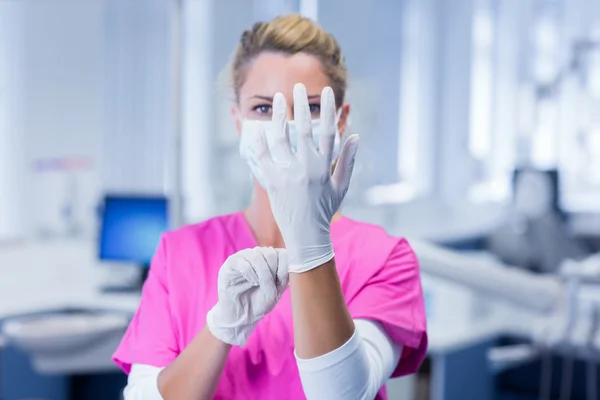 Dentist in pink scrubs putting on surgical gloves