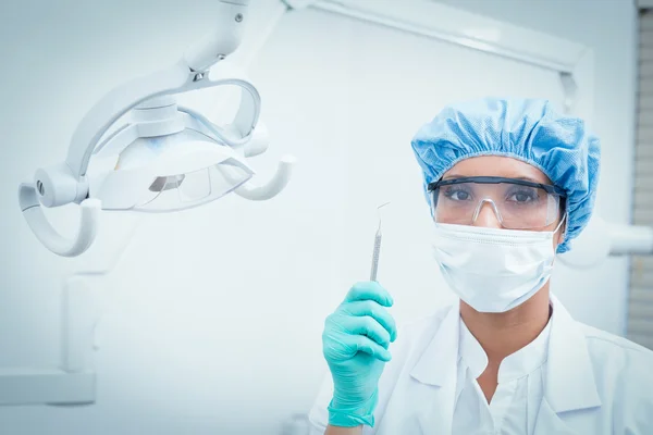 Dentist in surgical mask and safety glasses holding hook